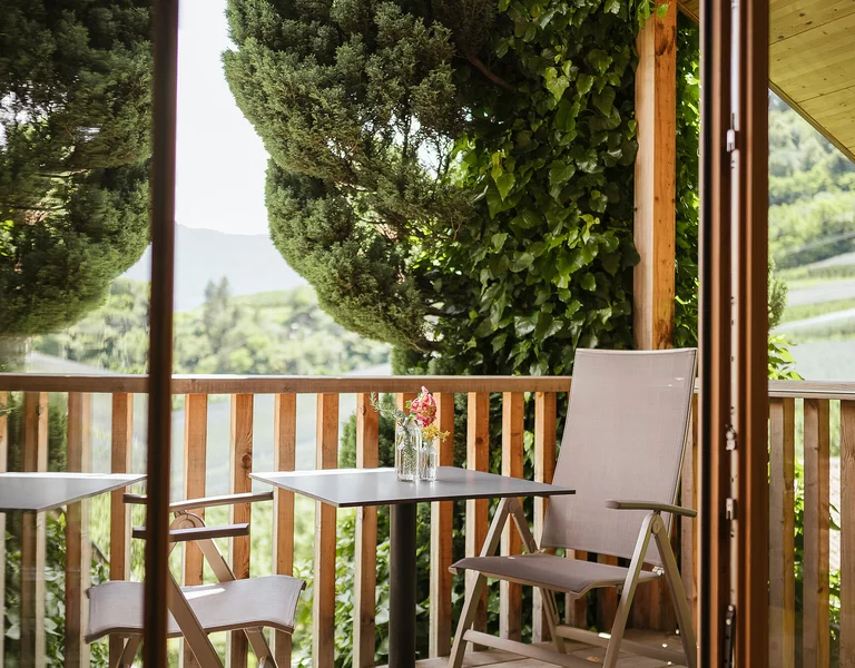 Balkon mit grünen Bäumen, Tisch und zwei Liegestühlen.